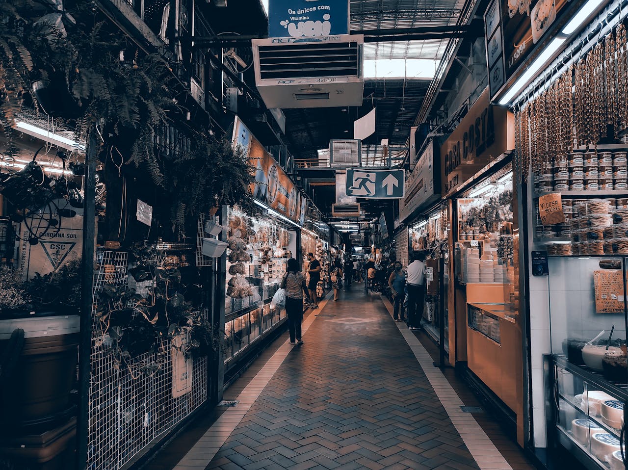 A vibrant indoor market scene with various stalls and shoppers exploring the goods on a busy pathway.